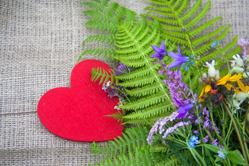 Red heart with bouquet from wildflowers and fern leafs on begging background. 