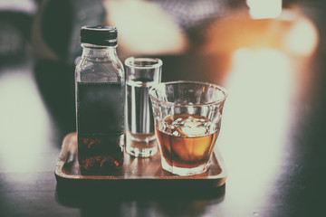 The abstract art design background of coffee bottle and glass of water on wooden tray,blurry light around.