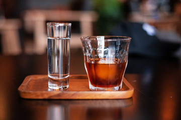 Coseup glass of cold coffee and glass of water put on wooden tray,blurry light around.