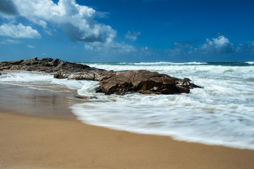 Rocks on the beach. Sky loaded with clouds on a deserted beach. Tropical paradise.