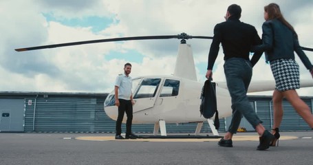 Commercial pilot in uniform greeting clients near small private helicopter on a landing point. 4K UHD
