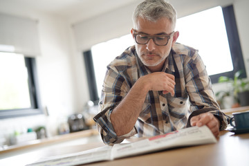 Middle-aged man in kitchen reading newspaper