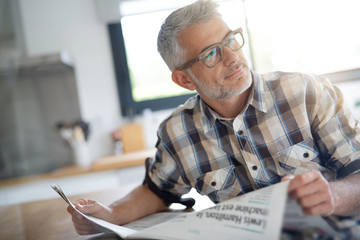 Middle-aged man in kitchen reading newspaper