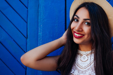 Fototapeta premium Happy middle-eastern girl smiling and looking at camera. Outdoor portrait of young woman wearing summer hat