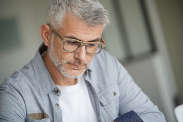 Middle-aged guy with trendy eyeglasses reading magazine