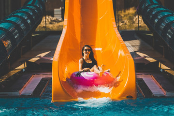 pretty girl in black bikini going down on the inflatable ring by the slide in the aqua park. Summer...