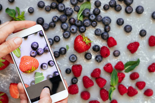 Photographing food. Hands taking picture of organic fresh harvested berries with smartphone