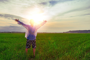 Boy spread his arms against the backdrop of the sun over soccer field. Back view. Landscape with a child raising his hands.