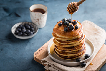 Stack of homemade pancakes with fresh blueberries and maple syrup on blue background