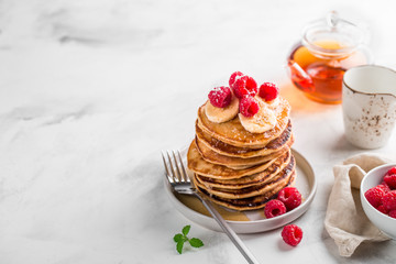 Stack of homemade pancakes with fresh raspberries on light marble background, copy space