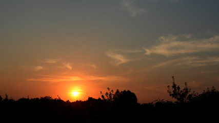 Fototapeta na wymiar Rays of sunset through dark clouds with a contour of trees on the horizon.