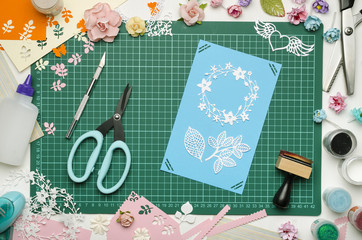 Multi-colored paper crafts on the cutting mat, tools and materials for scrapbooking, top view