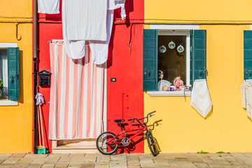 Naklejka premium Yellow and red house with a bicycle. Colorful houses in Burano island near Venice, Italy. Venice postcard. Famous place for european tourism and travel