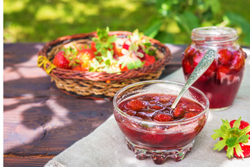 Strawberry jam and juicy ripe strawberries on a wooden table in the garden on a summer sunny afternoon in a rustic style, the concept of gardening, healthy organic vitamin nutrition