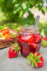 Strawberry jam and juicy ripe strawberries on a wooden table in the garden on a summer sunny afternoon in a rustic style, the concept of gardening, healthy organic vitamin nutrition