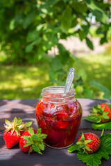 Strawberry jam and juicy ripe strawberries on a wooden table in the garden on a summer sunny afternoon in a rustic style, the concept of gardening, healthy organic vitamin nutrition