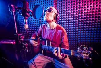 The singer sings with a microphone and playing guitar in the recording studio.