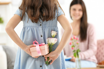 Little girl hiding gift and flowers for mommy behind her back on Mother's Day