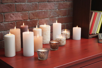 Many burning candles on wooden table against brick wall
