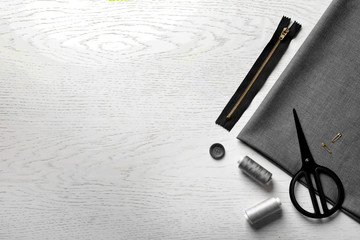 Set of tailoring accessories and fabric on light background, top view