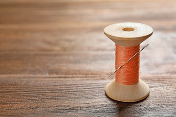 Spool of thread with needle on wooden background. Tailoring equipment