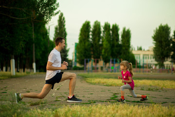 Athletic young father and little daughter do exercises in stadium. Healthy lifestyle