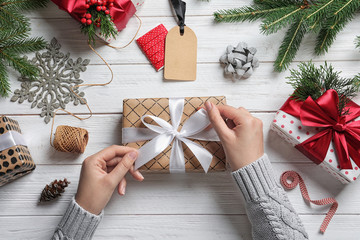 Woman wrapping Christmas gift at wooden table, top view - obrazy, fototapety, plakaty