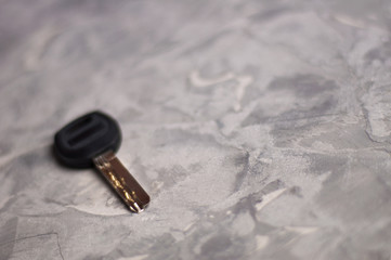One shiny metal key with black plastic handle on gray dirty scratched cement floor with copy space for your text. Security concept