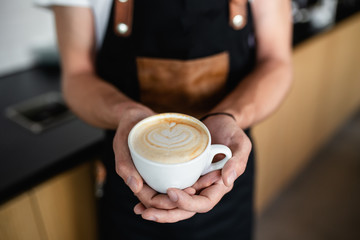 Professional barista holding cup of espresso coffee with milk.