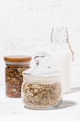 glass jar with oat flakes, granola and bottle of milk, vertical