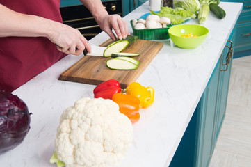 Man prepared vegetables for cooking vegetable ragout. Close up of cauliflower and paprika on white table. Man cutting zucchini and mushrooms