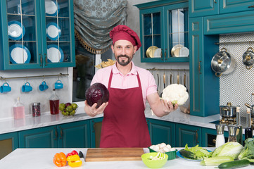 Cauliflower vs red cabbage to choose by chef. Man shows big Cauliflower and red cabbage before preparing and cutting for salad. Man holds vegetables in hands. Vegetables for ratatouille on table