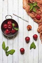 Close-up photo of  fresh red plum in a bowl. Top view on white vintage wooden background.