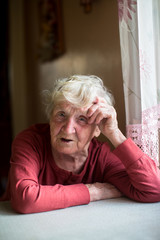 An elderly lady is sitting at the kitchen table.