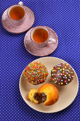 Baking with tea and chocolate on the table.  Two cups of tea with cupcakes and chocolate with a multicolored powder on the table.