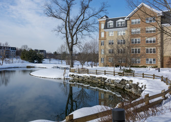 A mirror-like pond in front of a brick building with many windows in the middle of a wintry scene.