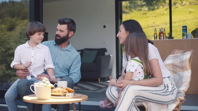 Nice little guy sitting on lap of dad, little girl sitting on lap of mom. Caucasian parents listening attentively to adorable kids. Countryside. Slavic family.