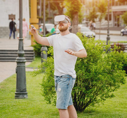 A young man plays a game wearing virtual reality glasses on the street.