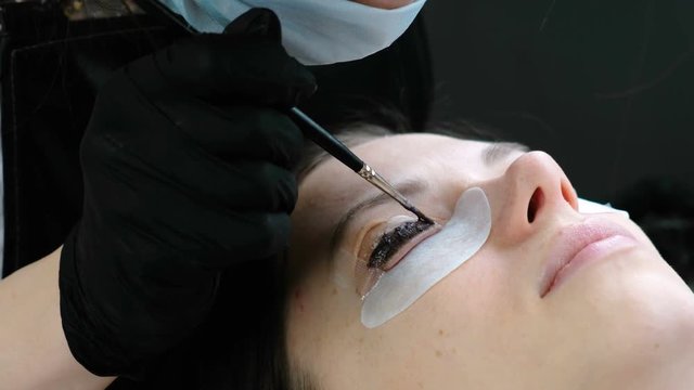 Beauty treatment. Cosmetologist puts black paint on the lashes. laminating eyelashes. Closeup face side view.