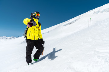 A portrait of a skier in a protective helmet and glasses is a mask and scarf with skis on his shoulder in the snow-capped mountains of the Caucasus. Skiing,