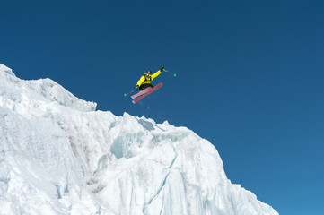 A jumping skier jumping from a glacier against a blue sky high in the mountains. Professional skiing