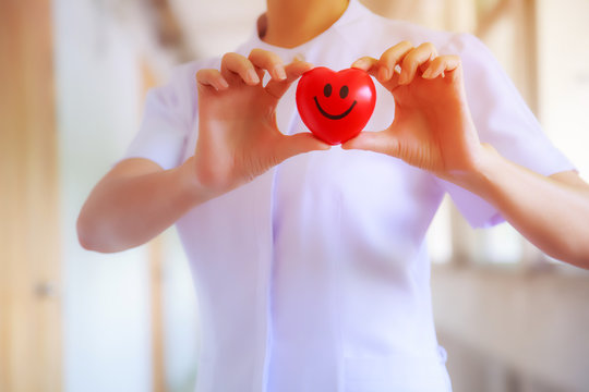 Red smiling heart held by female nurse's hand, representing giving effort high quality service mind to patient. Professional, Specialist in white uniform concept