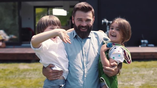 Nice cheerful Caucasian dad holding kids in hands. Father and children having fun, waving. Happy childhood. Outdoors. Countryside.
