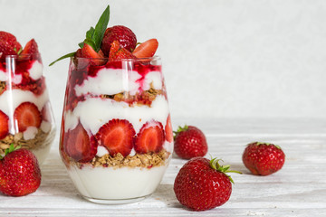 strawberry yogurt parfait with granola, mint and fresh berries in glasses on white wooden table.