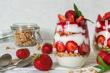 healthy fruit yogurt parfait with granola, mint and fresh raspberries in glasses on white wooden table