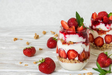 healthy strawberry yogurt parfait with granola, mint and fresh berries in glasses on white wooden table