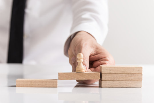 Businessman holding a pawn chess piece on a wooden block
