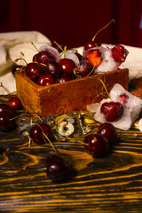 Frozen iced and fresh red cherry in a glass next to a vintage wooden box on an ancient wooden table on which spools of thread are scattered