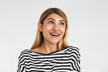 Studio portrait of adorable positive young Caucasian female with loose blonde hair looking up with cute charming smile, feeling shy and flattered while receiving compliment from her boyfriend