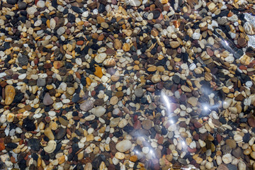 sea stones under blue water. Background of small multicolored stones lying under water.